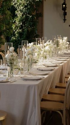 a long table is set up with white flowers and place settings for an elegant dinner