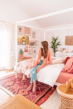 a woman sitting on top of a bed next to a pink couch in a bedroom