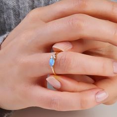 a woman's hand holding a ring with a blue opal stone on it