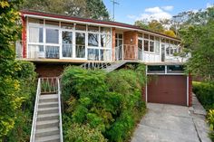 a house that is next to some trees and bushes with stairs leading up to it