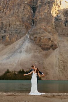 a bride and groom standing in front of a mountain lake