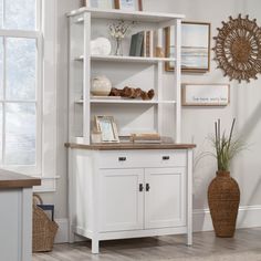 a white bookcase with doors and drawers in a room next to a potted plant