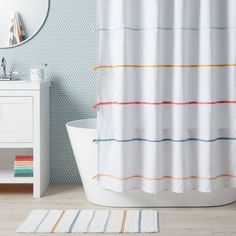 a white bath tub sitting next to a bathroom sink under a shower curtain with multicolored stripes on it