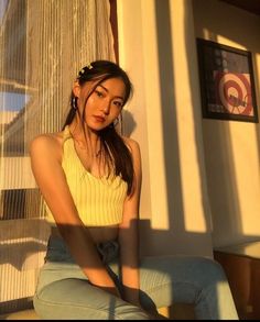 a beautiful young woman sitting on top of a wooden chair next to a window covered in sheer curtains