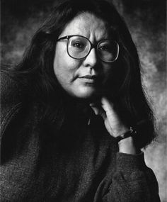 black and white photograph of a woman with glasses looking at the camera while leaning on her hand