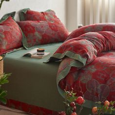 a bed with red and green comforters in a room next to a potted plant