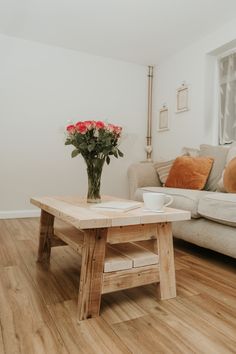 a coffee table with flowers on it in front of a white couch and wooden floor