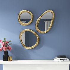 two mirrors on the wall above a table with vases and flowers in front of it