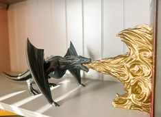 two metal dragon figurines sitting on top of a white shelf next to each other