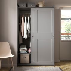 an open gray closet with clothes hanging on the door and two white chairs next to it