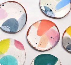 six plates with different colors on them sitting on a white table top, one has been painted and the other is made out of clay