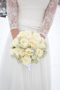 a bride holding a bouquet of white roses in her hands on the snow covered ground