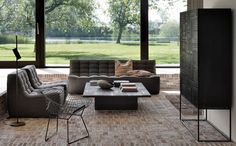 a living room filled with furniture next to large glass windows on top of a brick floor