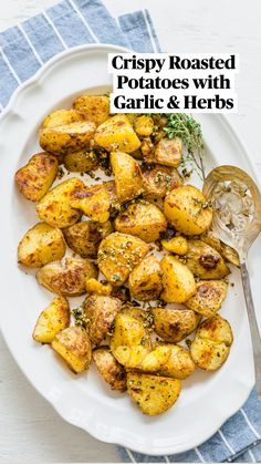 a white plate topped with potatoes covered in parmesan cheese and herbs next to a spoon