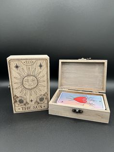 an open wooden box with the sun on it sitting next to a card game case