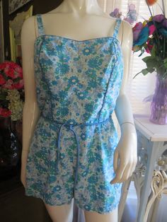 -style 1950s' floral one-piece romper style swimsuit by Perfection Fit/Rosanne, in a size 18/40.  Swimsuit has back metal zipper closure, skinny tie belt, small adjustable buttoned shoulder straps, slight pointy bust, blue front bodice trim, stretchy sides in the bodice backs, and fabric is cotton/Dacron/polyester. Swimsuit leg bottom has elastic under pants. Floral cotton fabric print is different sizes of daises in colors of teal, light green, white, and light blue.  Swimsuit is in good condition, but no padding in bra/bust area. WAIST=32-34"   BUST=36-38"/B cup   HIP=40-42"   THIGH=26-30"    PRICE IS $45.00-----SALE FINAL/AS IS/NO RETURNS. Retro Summer Floral Jumpsuits And Rompers, Retro Sleeveless Floral Print Jumpsuits, Retro Floral Print Sleeveless Jumpsuits, Retro Sleeveless Floral Jumpsuits And Rompers, Retro Floral Print Fitted Jumpsuits And Rompers, Vintage Floral Print Jumpsuits And Rompers, Retro Fitted Floral Print Jumpsuits And Rompers, Vintage Floral Print Jumpsuit For Spring, Fitted Vintage Floral Print Jumpsuits And Rompers