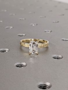 a gold ring with an emerald cut diamond in the center on a silver surface surrounded by small dots