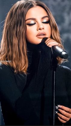 a woman with long hair holding a microphone in front of her face and looking into the distance