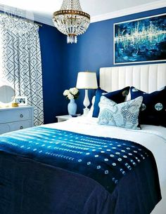 a blue and white bedroom with chandelier, bed, nightstands and pictures on the wall