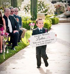 a young boy in a suit and tie running down a sidewalk holding a sign that says don't worry ladies, i am may be just but i'm still single