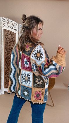 a woman standing in front of a fireplace wearing a multicolored crocheted sweater