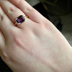 a woman's hand wearing a gold ring with an amethorate stone