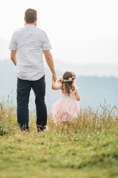 a father and daughter holding hands while standing on top of a hill