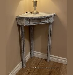 a table with a lamp on top of it next to a white wall and wooden floor