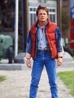 a man in jeans and a vest standing on a sidewalk