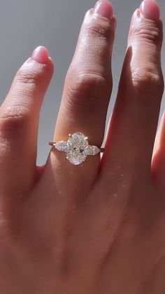 a woman's hand with a diamond ring on top of her finger and the other hand holding an engagement ring