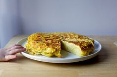 a person reaching for a piece of omelet on a plate with one slice cut out