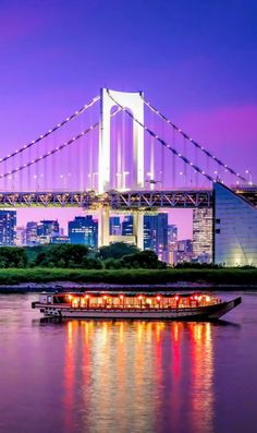 a bridge that is over some water with buildings in the background and lights on it