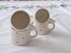 two coffee mugs with the words love you mum printed on them sitting on a bed