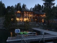 a house is lit up at night on the water's edge with boats docked in front