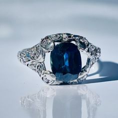 an oval blue stone surrounded by filigree leaves on a white surface with reflection