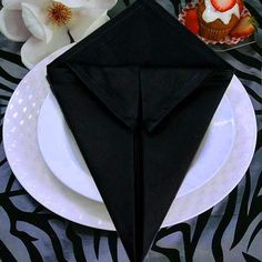 a black napkin folded over a white plate on a zebra print table cloth with cupcakes and flowers in the background