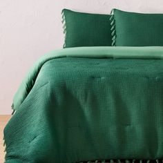 a bed with green sheets and pillows on top of wooden floor next to white wall