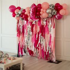 balloons and streamers are hanging from the wall in this room with pink, silver and white decor