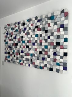 a wall hanging made out of several different colored squares on the side of a white wall