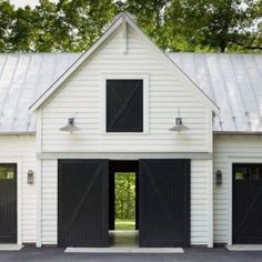 two garages with black doors are in the middle of a driveway and trees behind them