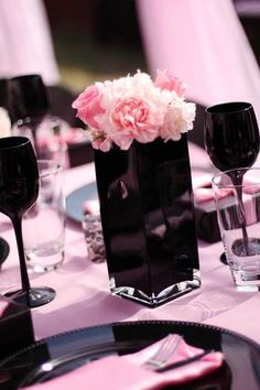 a black vase filled with pink and white flowers on top of a purple table cloth