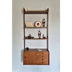 a shelf with books, vases and other items on it against a white wall