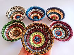 a hand is holding a colorful bowl in front of six bowls with designs on them