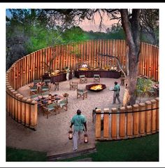 two men standing in front of a fire pit surrounded by wooden fenced area with chairs and tables