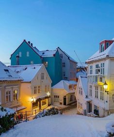 the snow covered streets and buildings are lit up by street lamps at dusk in an old european town