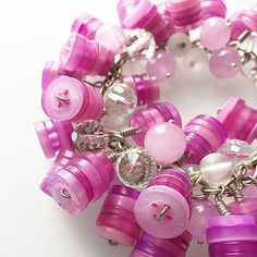 pink and purple bracelet with buttons and chains on white table top next to bottle openers