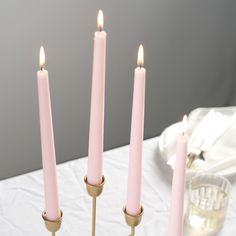 pink candles are lined up on a white table cloth with gold accents and glass dishes in the background