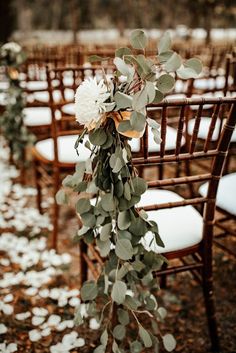 an outdoor ceremony set up with white flowers and greenery on the back of chairs