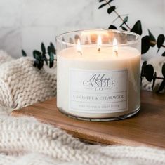 a candle sitting on top of a wooden table next to a white sweater and plant