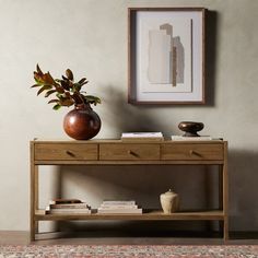 a wooden table topped with a vase filled with flowers next to a framed art piece